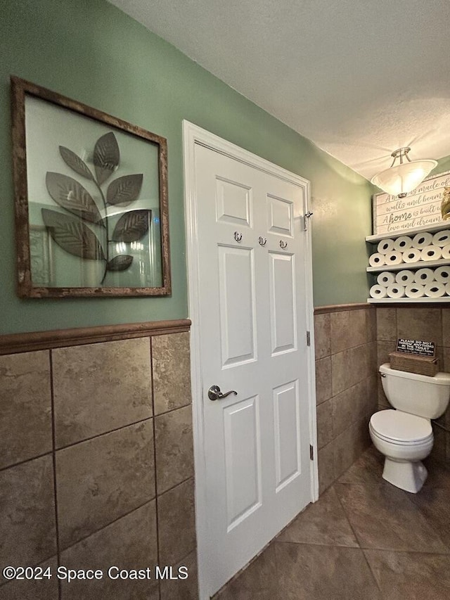 bathroom featuring a textured ceiling, tile patterned flooring, tile walls, and toilet