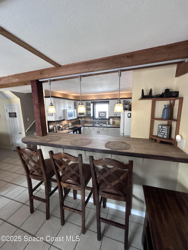 kitchen featuring kitchen peninsula, white appliances, hanging light fixtures, and a breakfast bar area