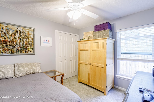 bedroom featuring a textured ceiling, light colored carpet, ceiling fan, and a closet