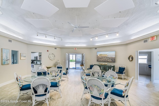 dining space featuring ceiling fan, rail lighting, a textured ceiling, a tray ceiling, and light wood-type flooring