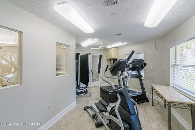 workout area with ceiling fan, light hardwood / wood-style floors, and a textured ceiling