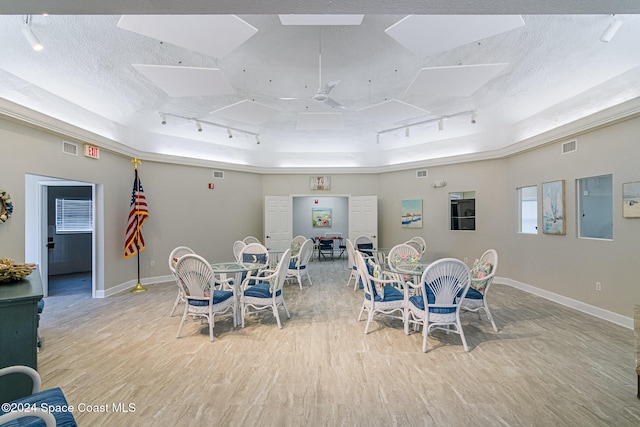 dining area featuring track lighting, ceiling fan, light wood-type flooring, a textured ceiling, and a tray ceiling