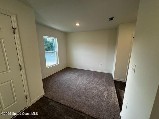 unfurnished bedroom with dark colored carpet, dark wood finished floors, visible vents, and baseboards