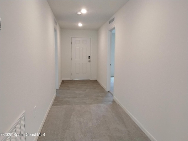 hallway featuring light carpet, visible vents, and baseboards