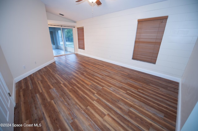 unfurnished room with ceiling fan, vaulted ceiling, wood walls, and dark hardwood / wood-style floors