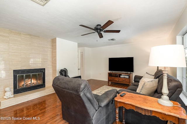 living room with ceiling fan, a fireplace, a textured ceiling, and hardwood / wood-style flooring