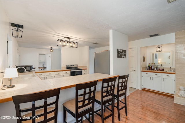 kitchen featuring tile counters, light hardwood / wood-style flooring, kitchen peninsula, a breakfast bar, and appliances with stainless steel finishes