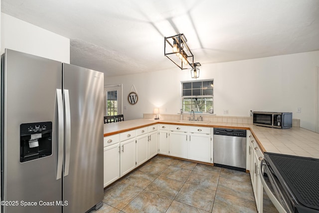 kitchen featuring tile counters, sink, kitchen peninsula, white cabinets, and appliances with stainless steel finishes