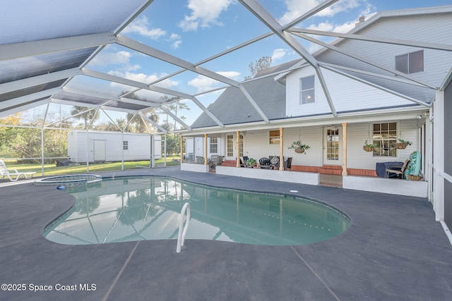 view of pool with glass enclosure, a patio area, an in ground hot tub, and a shed