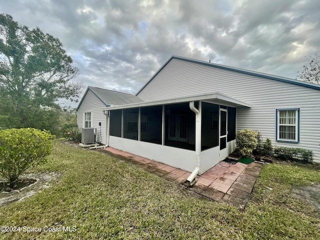 back of property featuring central air condition unit, a lawn, and a sunroom