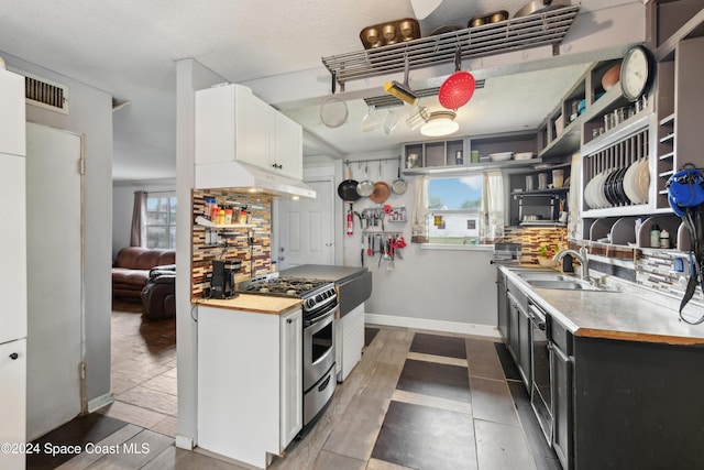 kitchen with backsplash, stainless steel gas range, a healthy amount of sunlight, sink, and white cabinetry