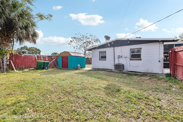 back of house with a lawn, central AC unit, and a storage shed