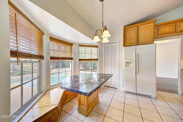 kitchen featuring a center island, white refrigerator with ice dispenser, dark stone countertops, a chandelier, and light tile patterned floors