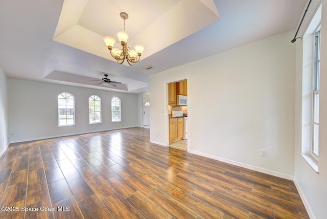 unfurnished living room featuring dark hardwood / wood-style flooring, ceiling fan with notable chandelier, and a raised ceiling