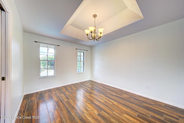 empty room featuring a notable chandelier, dark hardwood / wood-style floors, and a tray ceiling