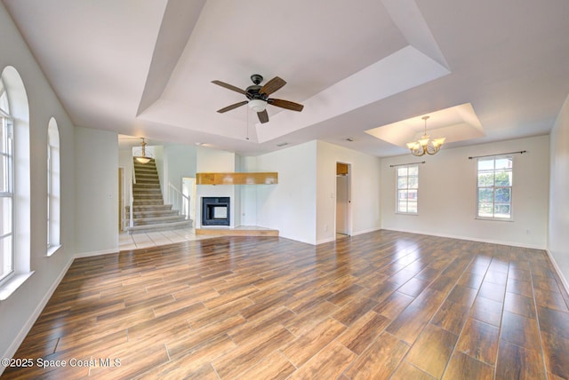 unfurnished living room with ceiling fan with notable chandelier and a tray ceiling