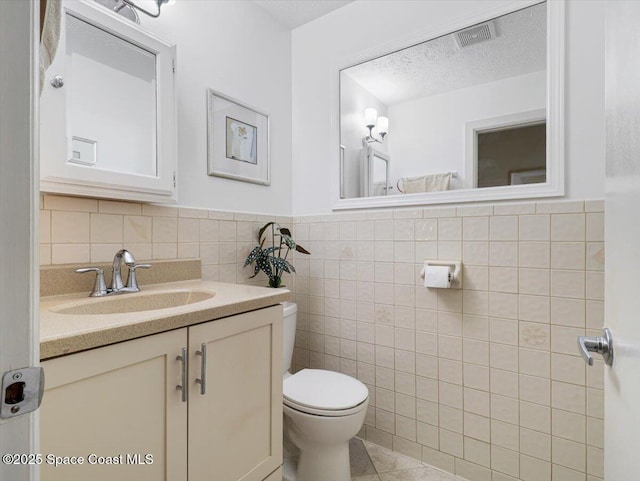 bathroom with vanity, tile patterned flooring, toilet, a textured ceiling, and tile walls