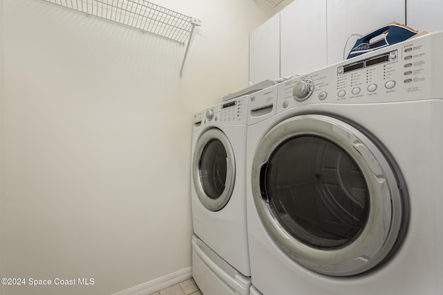 clothes washing area featuring cabinets, washing machine and dryer, and light tile patterned floors