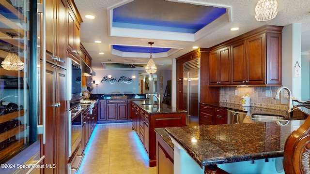 kitchen with a center island with sink, pendant lighting, sink, and a tray ceiling