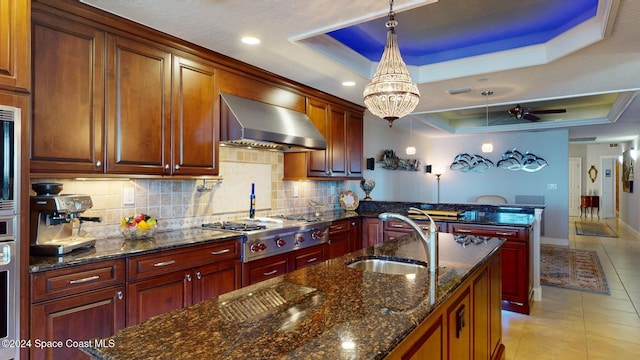 kitchen with pendant lighting, sink, wall chimney exhaust hood, appliances with stainless steel finishes, and a tray ceiling