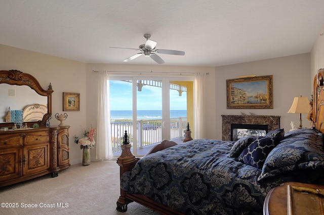 carpeted bedroom featuring access to outside, a water view, ceiling fan, a beach view, and a premium fireplace