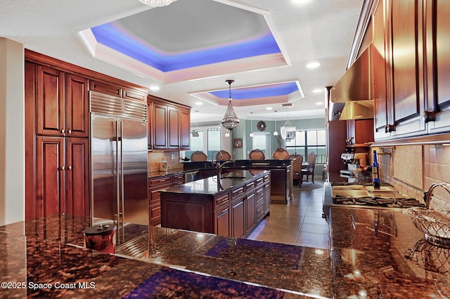 kitchen featuring decorative light fixtures, built in refrigerator, a raised ceiling, and sink