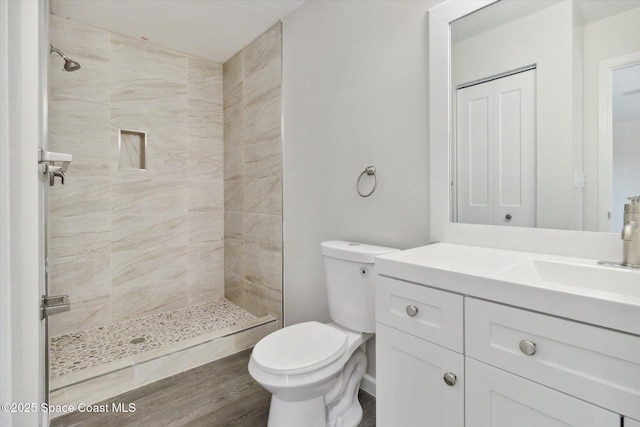 bathroom featuring hardwood / wood-style floors, toilet, a tile shower, and vanity