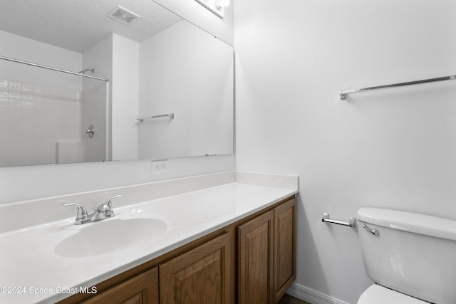 bathroom with a textured ceiling, vanity, toilet, and walk in shower