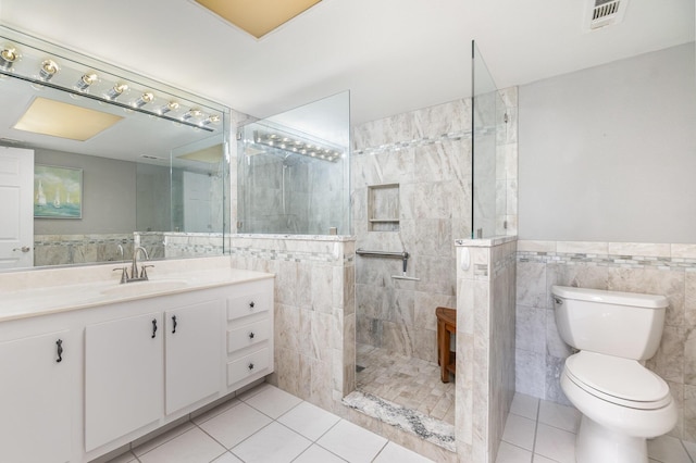 bathroom featuring toilet, tiled shower, tile patterned floors, and tile walls