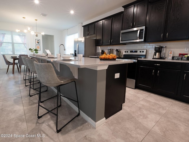 kitchen featuring a chandelier, a kitchen island with sink, stainless steel appliances, and decorative light fixtures