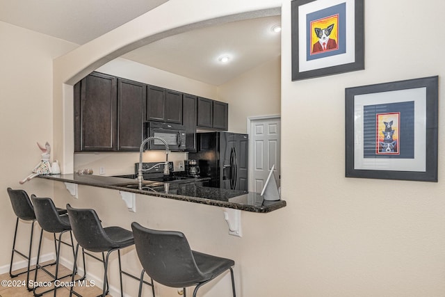 kitchen with black appliances, dark brown cabinets, a kitchen bar, and dark stone counters