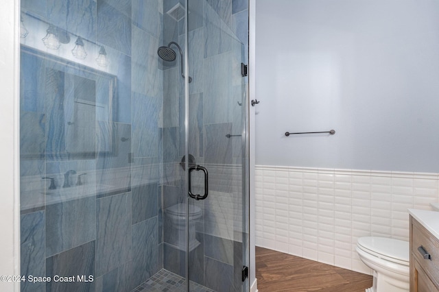 bathroom featuring vanity, toilet, a shower with door, and tile walls