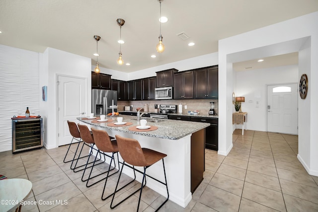 kitchen with beverage cooler, stainless steel appliances, pendant lighting, a breakfast bar area, and a kitchen island with sink