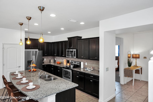 kitchen featuring light stone countertops, stainless steel appliances, sink, a center island with sink, and hanging light fixtures