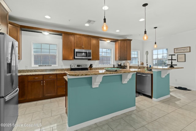 kitchen featuring a kitchen bar, light stone countertops, stainless steel appliances, a kitchen island with sink, and hanging light fixtures