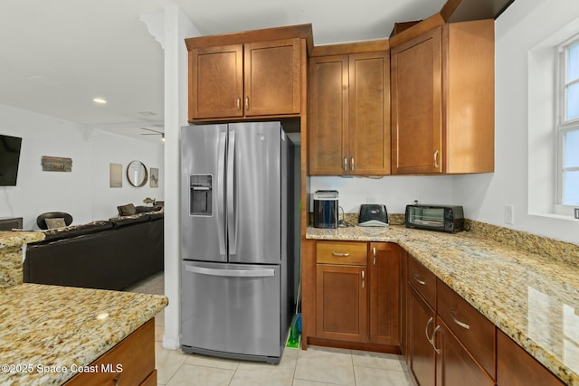 kitchen featuring ceiling fan, stainless steel fridge, light stone counters, and light tile patterned floors