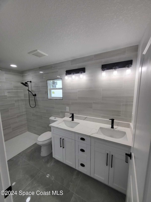 bathroom with vanity, toilet, a tile shower, and a textured ceiling