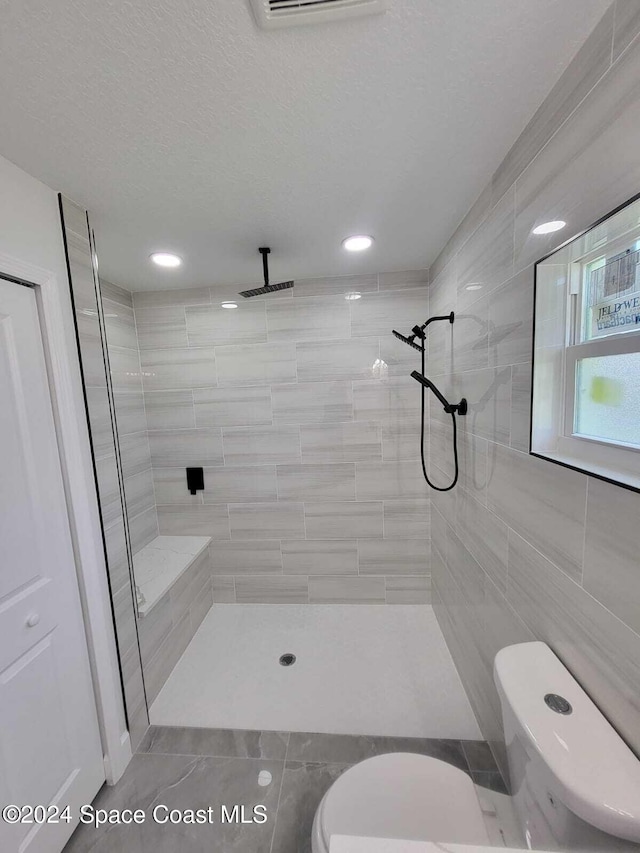 bathroom with tiled shower, a textured ceiling, and toilet