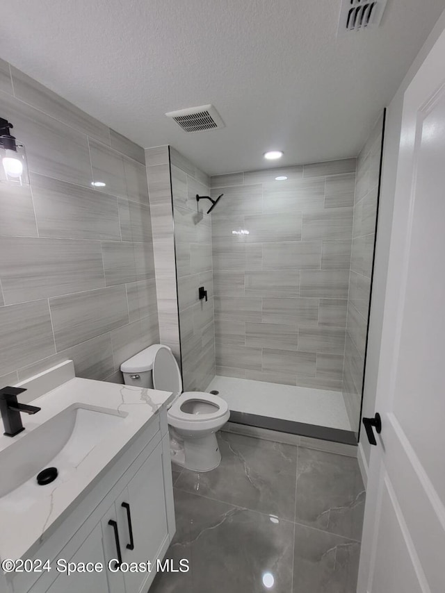 bathroom with vanity, toilet, tiled shower, a textured ceiling, and tile walls