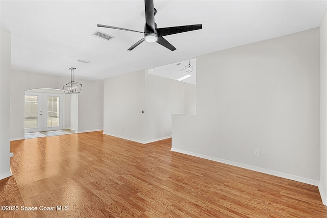 unfurnished living room with ceiling fan with notable chandelier, french doors, and light hardwood / wood-style floors