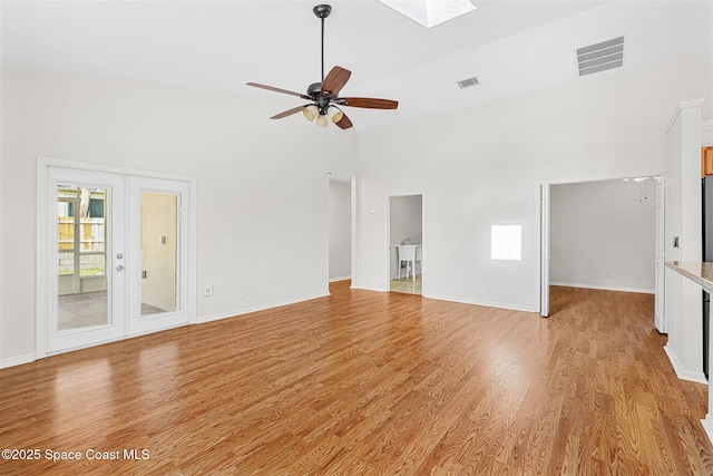 unfurnished living room featuring a skylight, french doors, ceiling fan, and light hardwood / wood-style floors