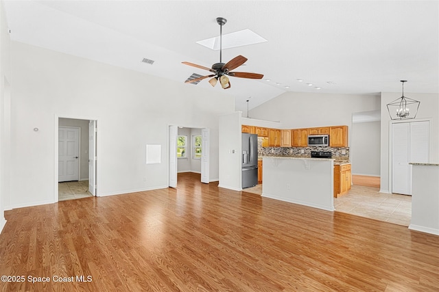 unfurnished living room featuring ceiling fan with notable chandelier, high vaulted ceiling, and light hardwood / wood-style floors