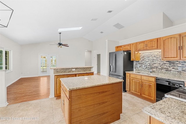 kitchen featuring dishwasher, stainless steel fridge, lofted ceiling with skylight, a kitchen island, and backsplash