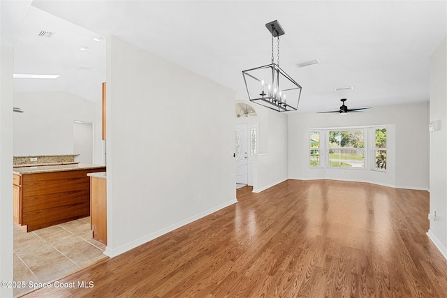 unfurnished living room featuring ceiling fan with notable chandelier, light wood-type flooring, and vaulted ceiling