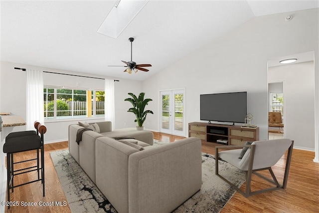 living room featuring light wood-type flooring, ceiling fan, lofted ceiling with skylight, and a healthy amount of sunlight