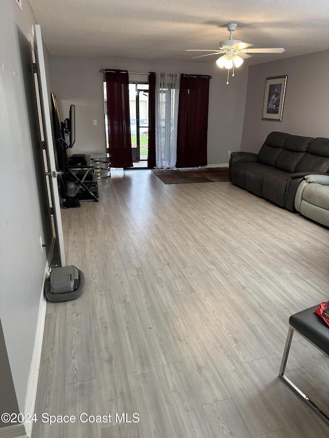 living room with ceiling fan, light wood-type flooring, and a textured ceiling