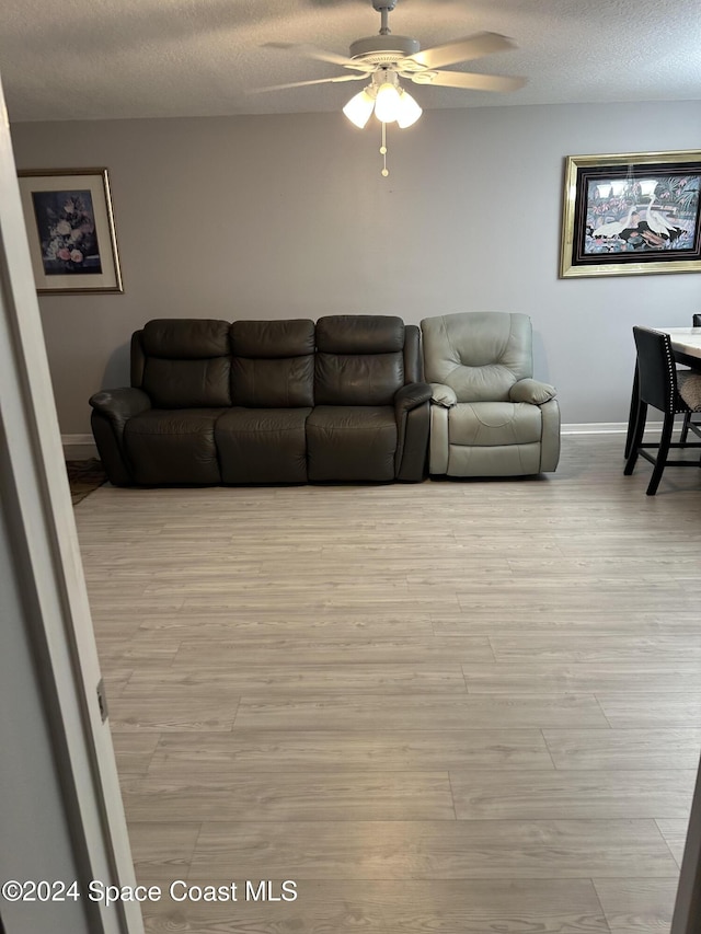 living room with a textured ceiling, light wood-type flooring, and ceiling fan