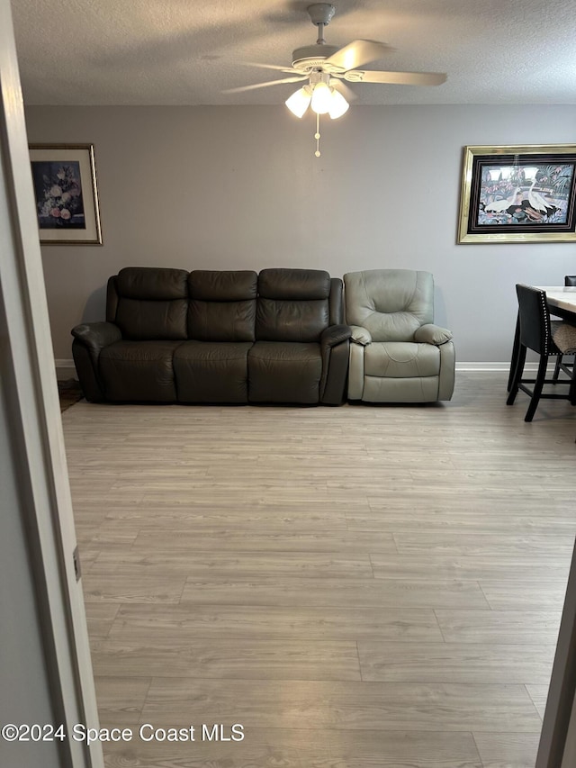 living room featuring ceiling fan, a textured ceiling, and light hardwood / wood-style flooring