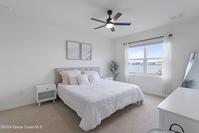 bedroom with light carpet, a water view, and ceiling fan