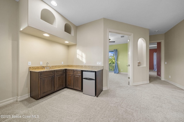 kitchen featuring light stone countertops, sink, fridge, light carpet, and dark brown cabinets